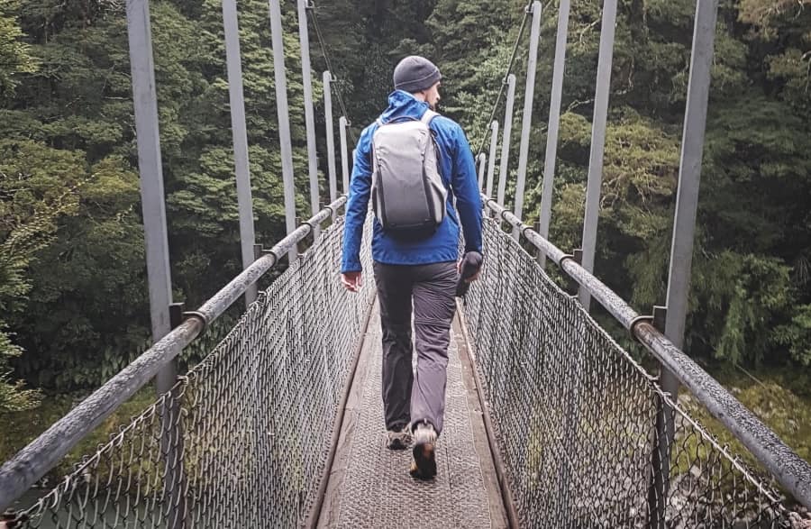 picture of Will walking across a swing bridge, holding a camera tripod